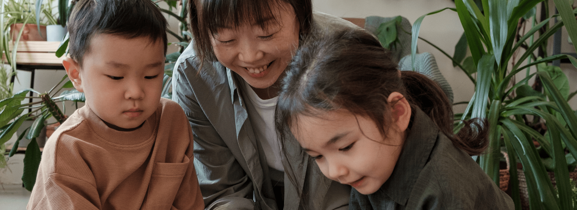 Un adulte joue avec deux enfants dans un décor avec des plantes.