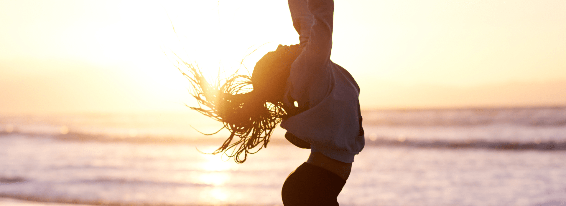 Une femme qui saute de joie sur la plage avec un coucher de soleil.